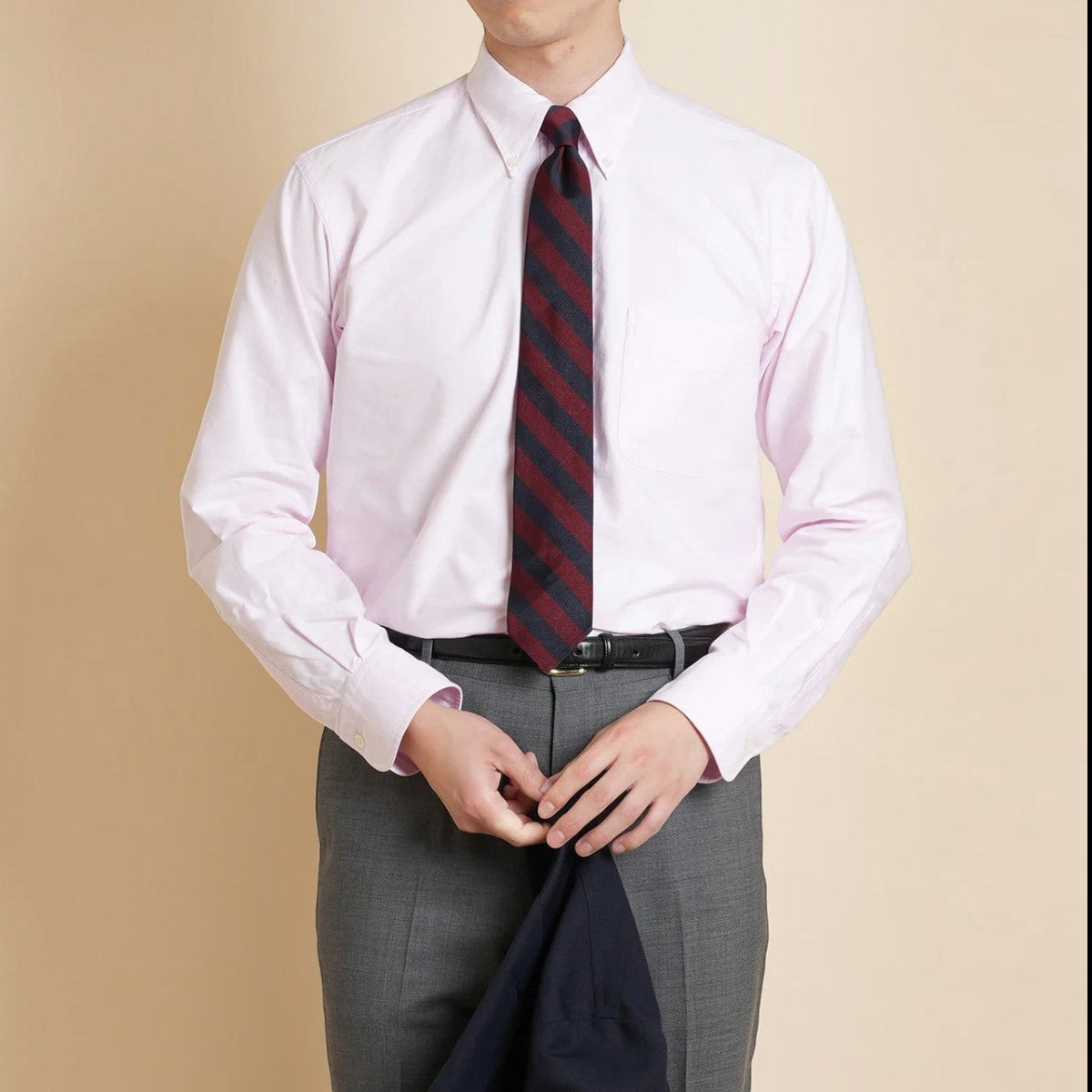 A man wearing a Kamakura pink cotton oxford button-down shirt with a striped tie and grey trousers.