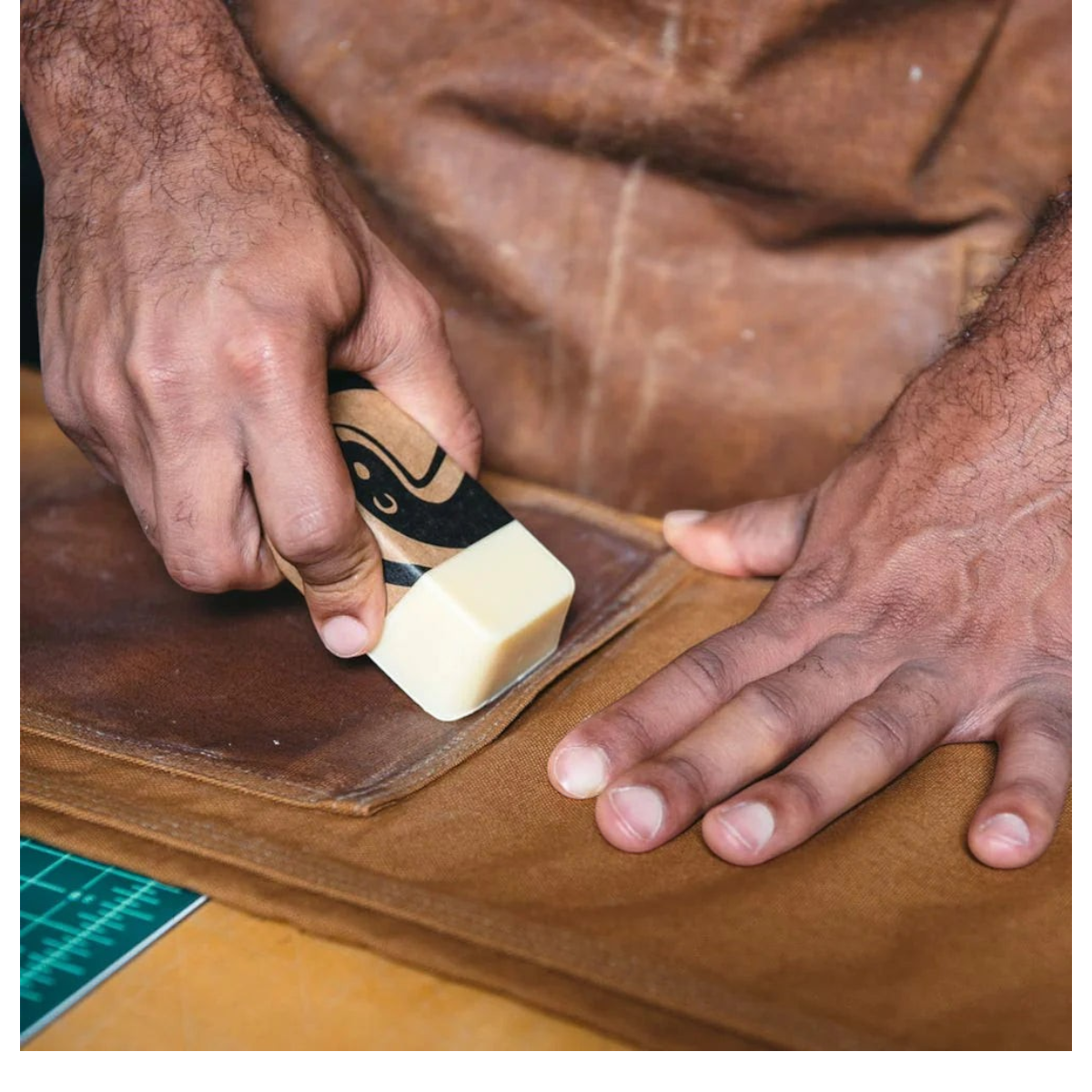 MILWORKS Otter Wax heavy duty fabric wax bar being applied to brown canvas fabric for water-resistant protection.