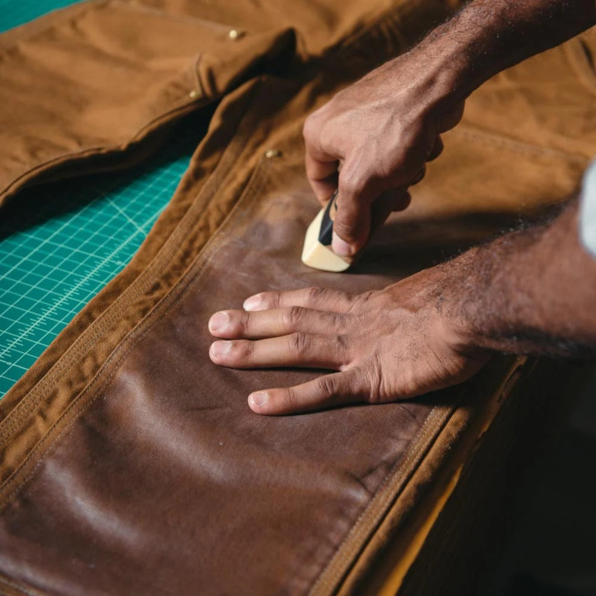 MILWORKS Otter Wax heavy duty fabric wax bar being applied to brown canvas pants for water-resistant protection.
