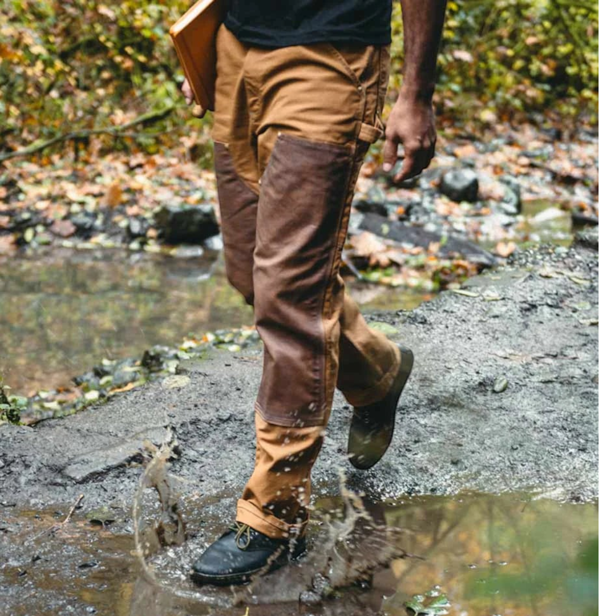 MILWORKS model wearing brown canvas work pants with reinforced dark brown patches walking through a muddy puddle
