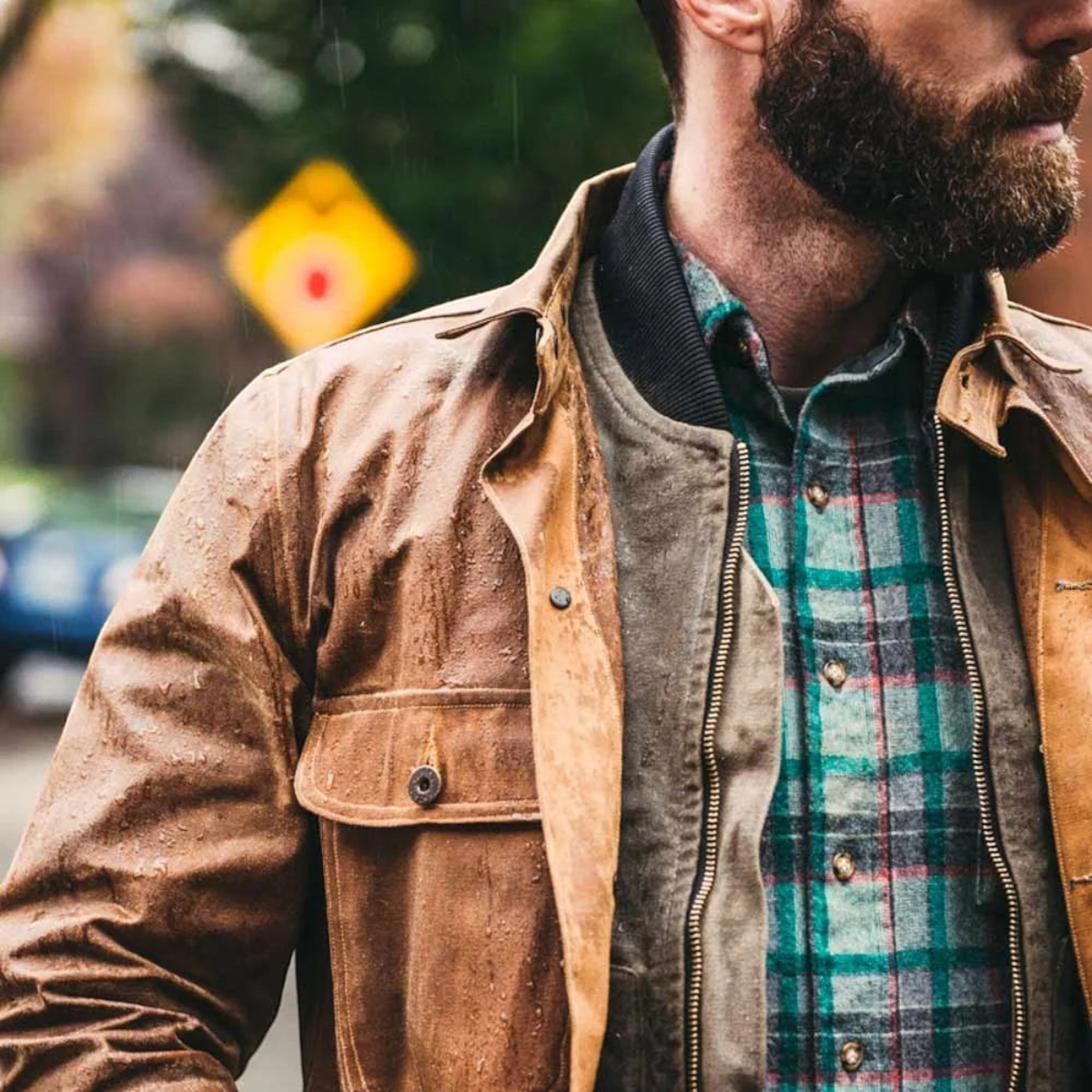 MILWORKS Otter Wax heavy duty fabric wax applied to a brown waxed canvas jacket worn by a man in the rain