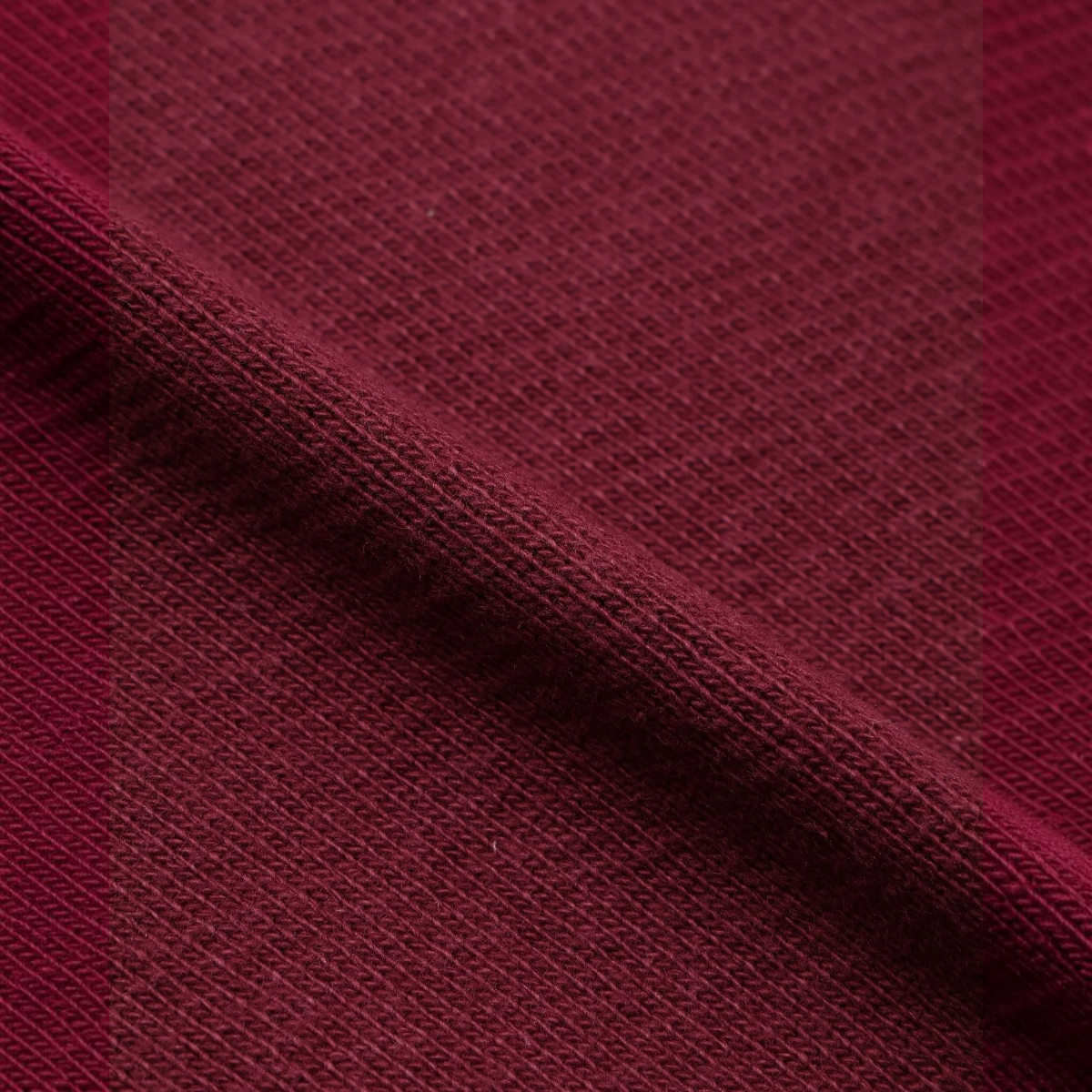 Close-up of MILWORKS burgundy double heavyweight French terry cotton fabric with a dense, textured knit surface.