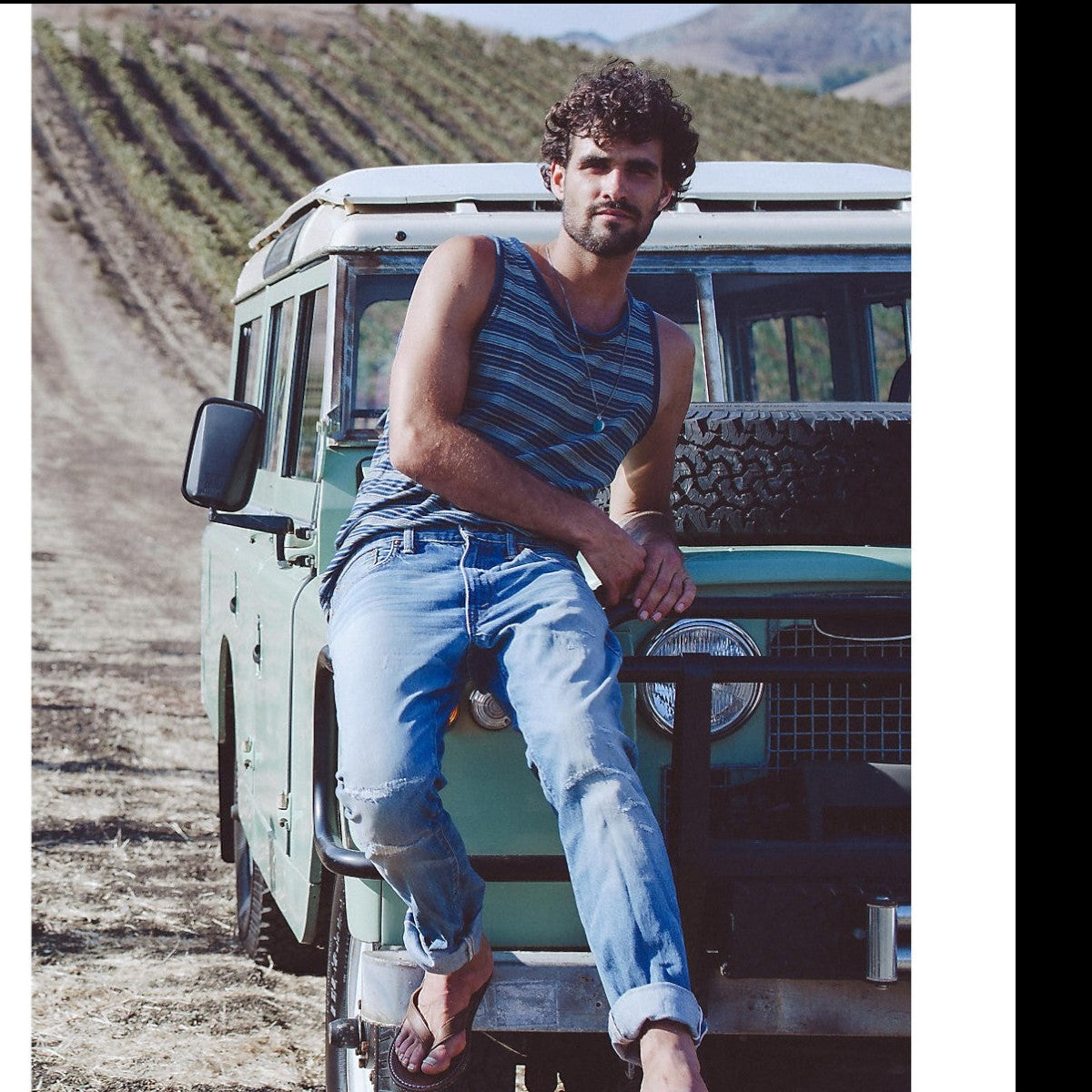 MILWORK Indigo Multi Striped Cotton Jersey Tank with ribbed trim on a man sitting on a vintage vehicle.