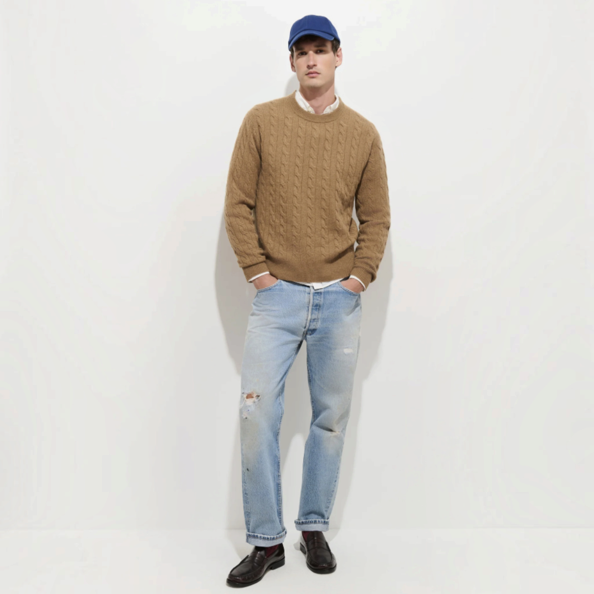 MILWORKS model wearing a cocoa brown 100% cashmere cable knit sweater with a blue cap and light wash distressed jeans.