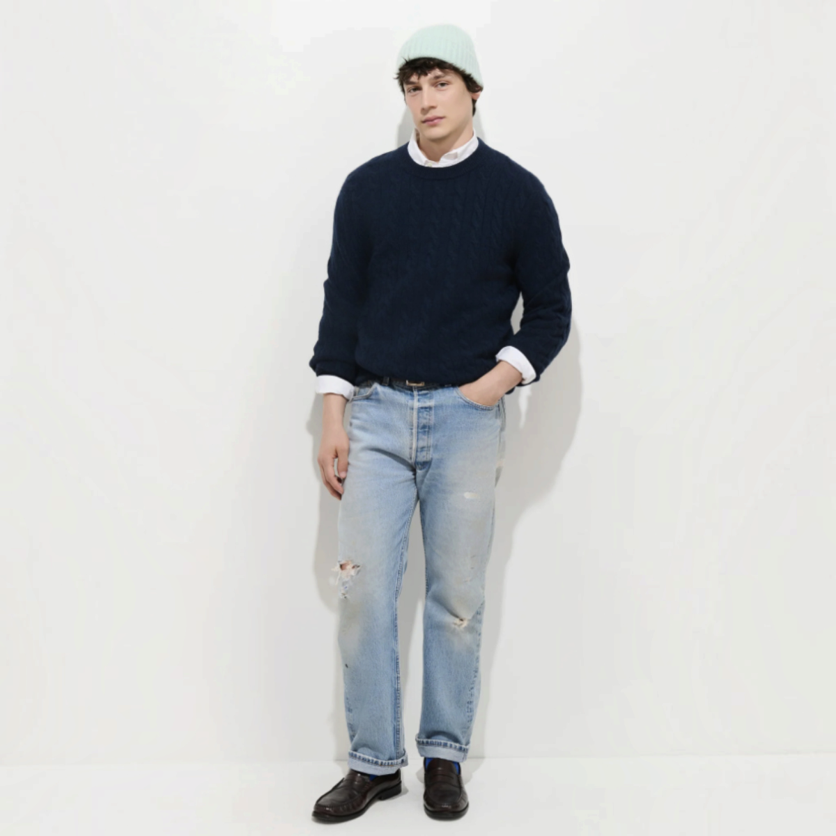 MILWORKS model wearing a navy blue 100% cashmere cable knit sweater with a white shirt and light wash distressed jeans