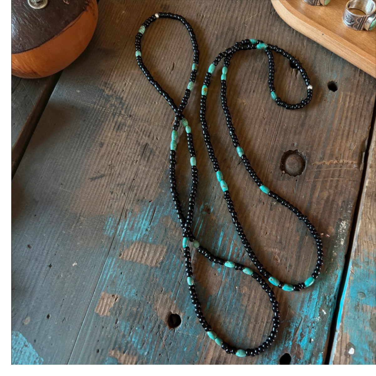 MILWORKS 26-inch necklace with black seed beads and genuine turquoise accents on a rustic wooden table