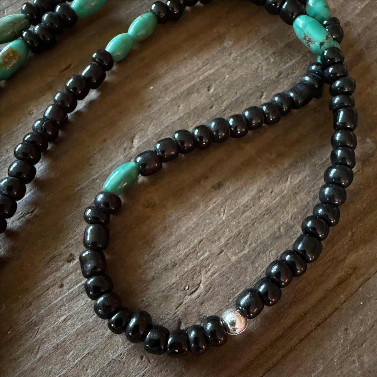 MILWORKS black seed bead and genuine turquoise necklace with a sterling silver crimp bead on a rustic wood surface.