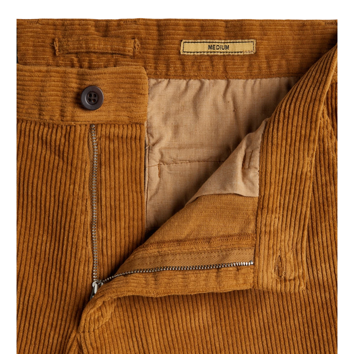 MILWORKS corduroy trousers in a warm autumn brown featuring a single pleat, metal zipper, and recycled button detail.