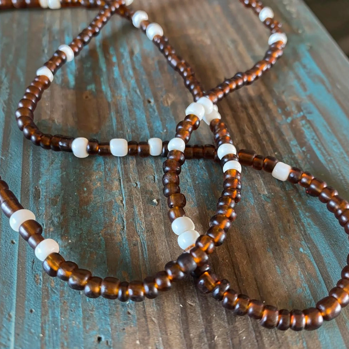 MILWORKS chocolate glass trade bead necklace with white seed bead accents on a rustic blue wooden surface