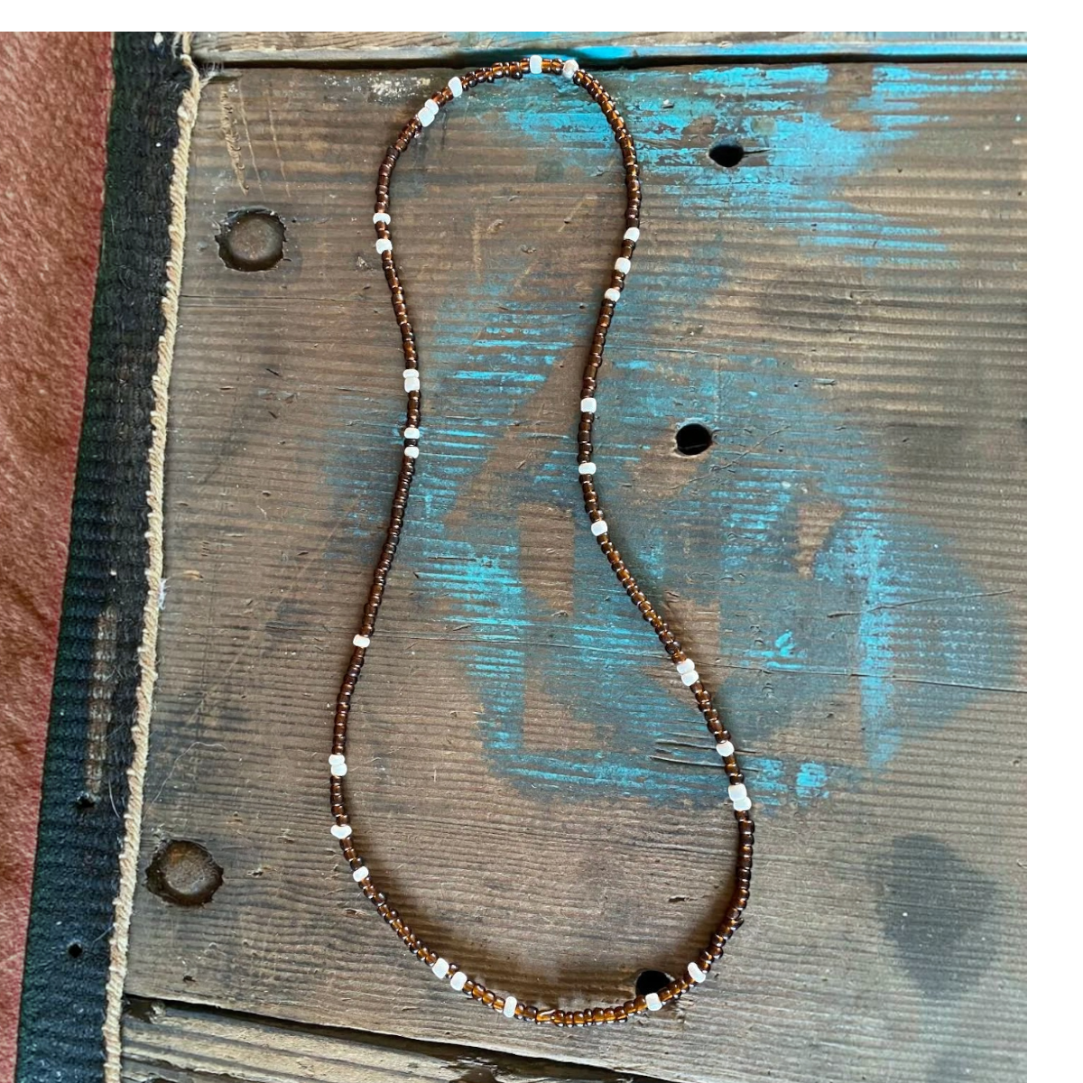 MILWORKS chocolate brown glass trade bead necklace with white seed bead accents on a rustic wooden surface