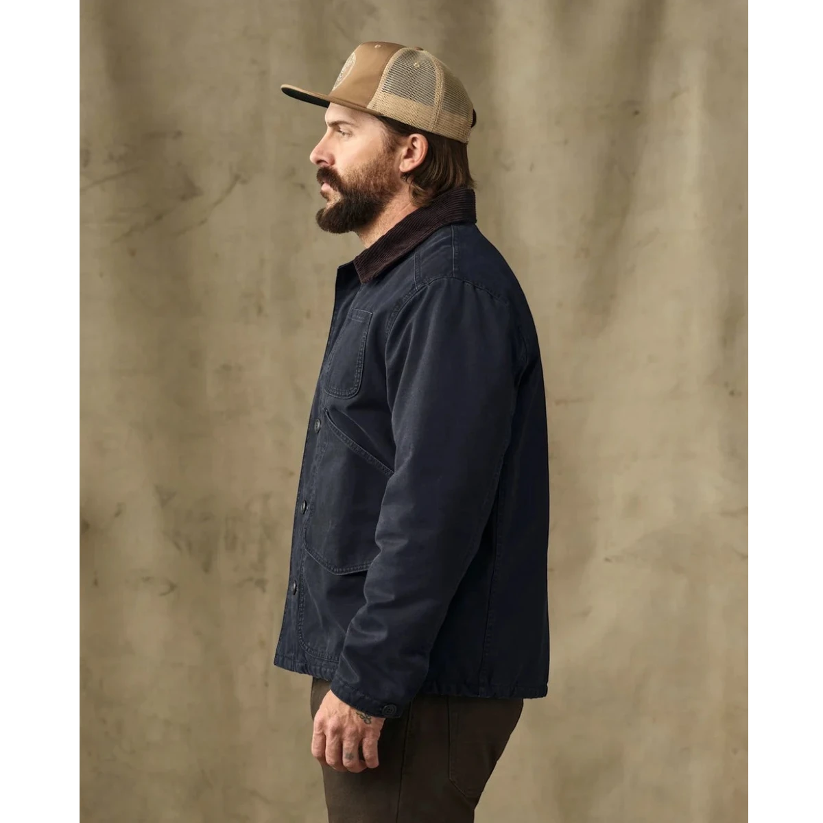 MILWORKS model wearing a dark navy insulated canvas outfitter jacket with a corduroy collar, side profile view.