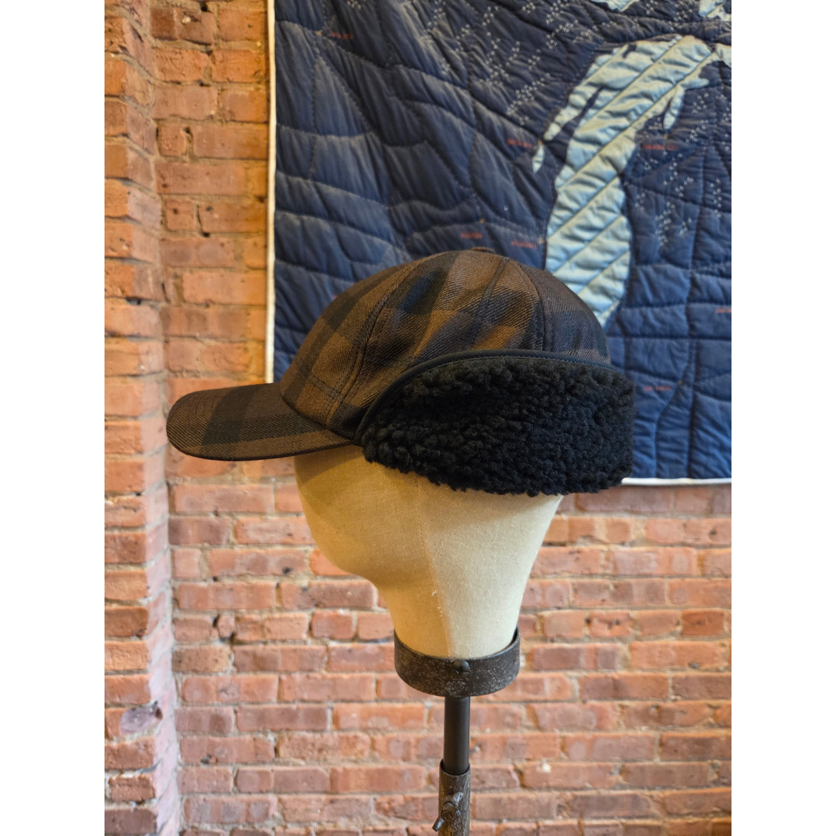 MILWORKS EG hunting cap in brown and black worsted wool plaid with black fleece ear flaps on a mannequin head