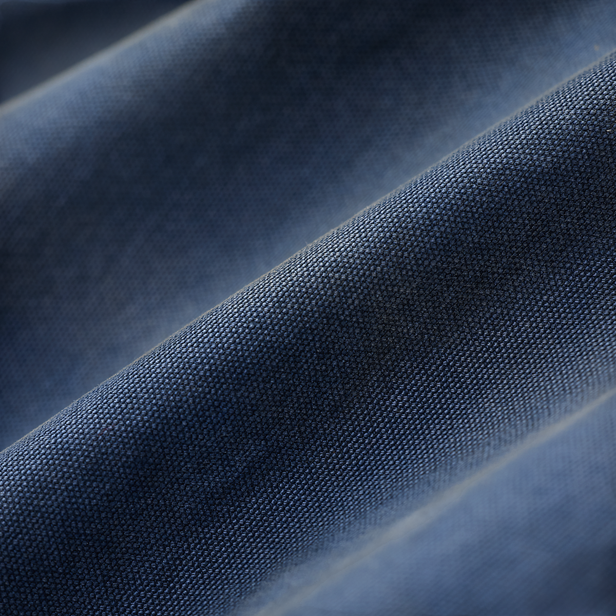 Close-up of MILWORKS faded navy 12 oz. cotton canvas fabric with a textured, lived-in vintage appearance.