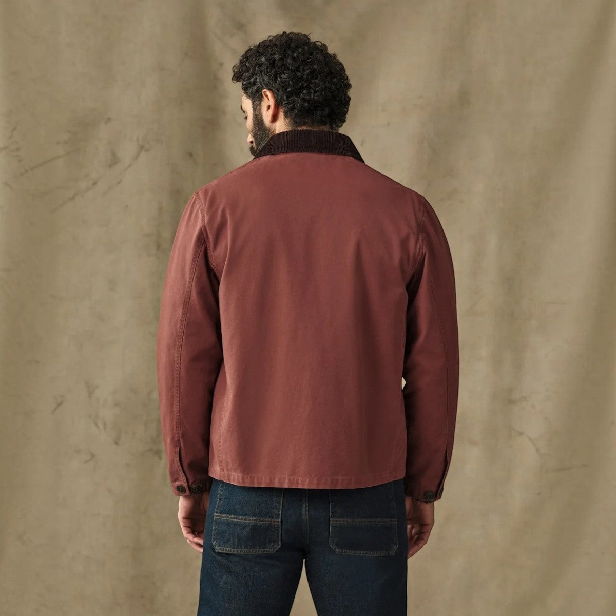 Back view of a man wearing a MILWORKS Filson Canvas Outfitter Jacket in Sequoia red with a corduroy-lined collar.
