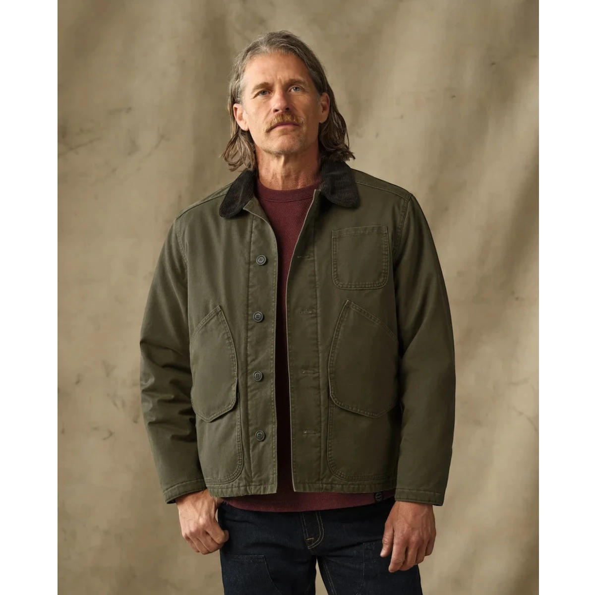 MILWORKS Filson dark olive insulated canvas outfitter jacket with corduroy collar worn by a man in a studio setting.