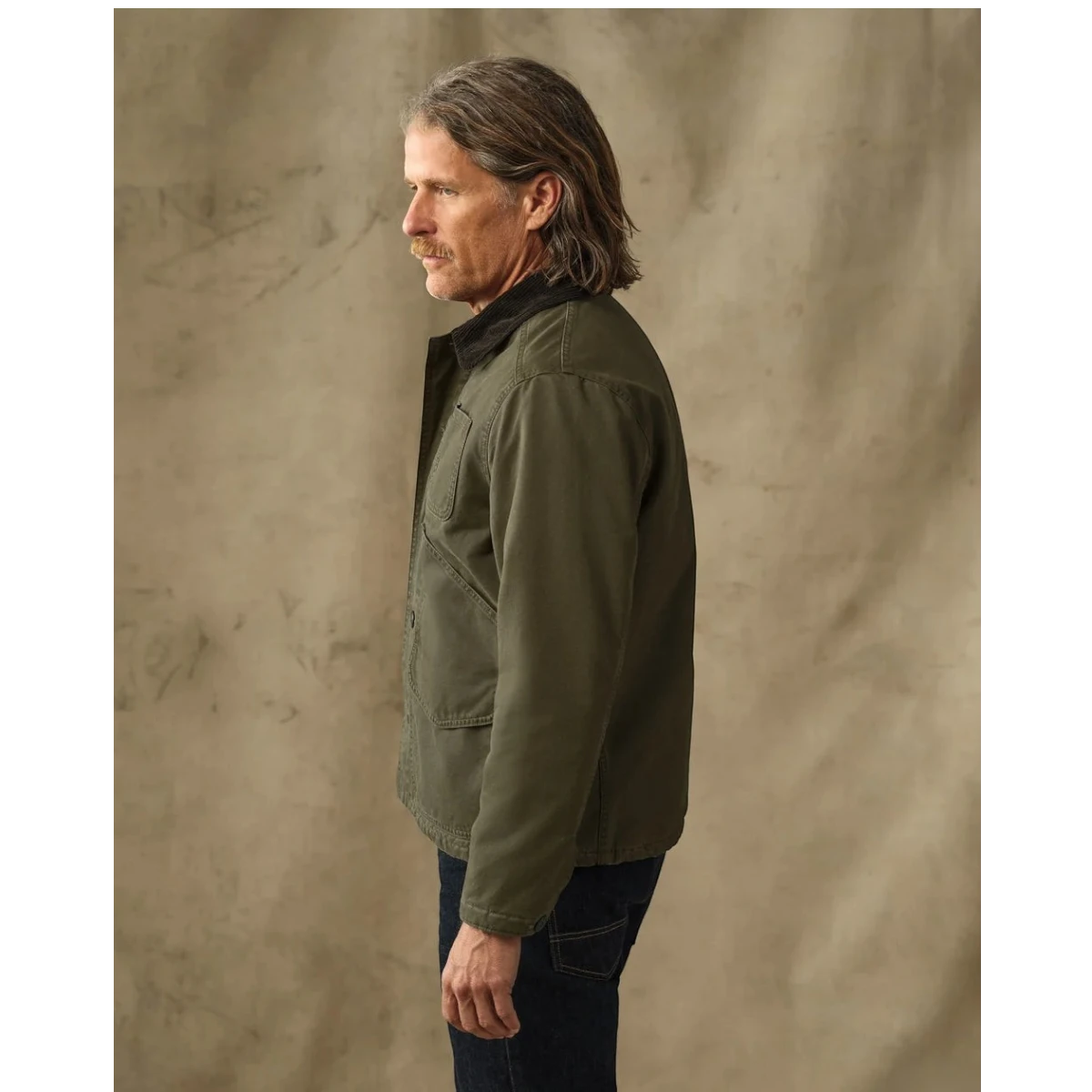 MILWORKS Filson dark olive insulated canvas outfitter jacket with corduroy collar worn by a man in profile view