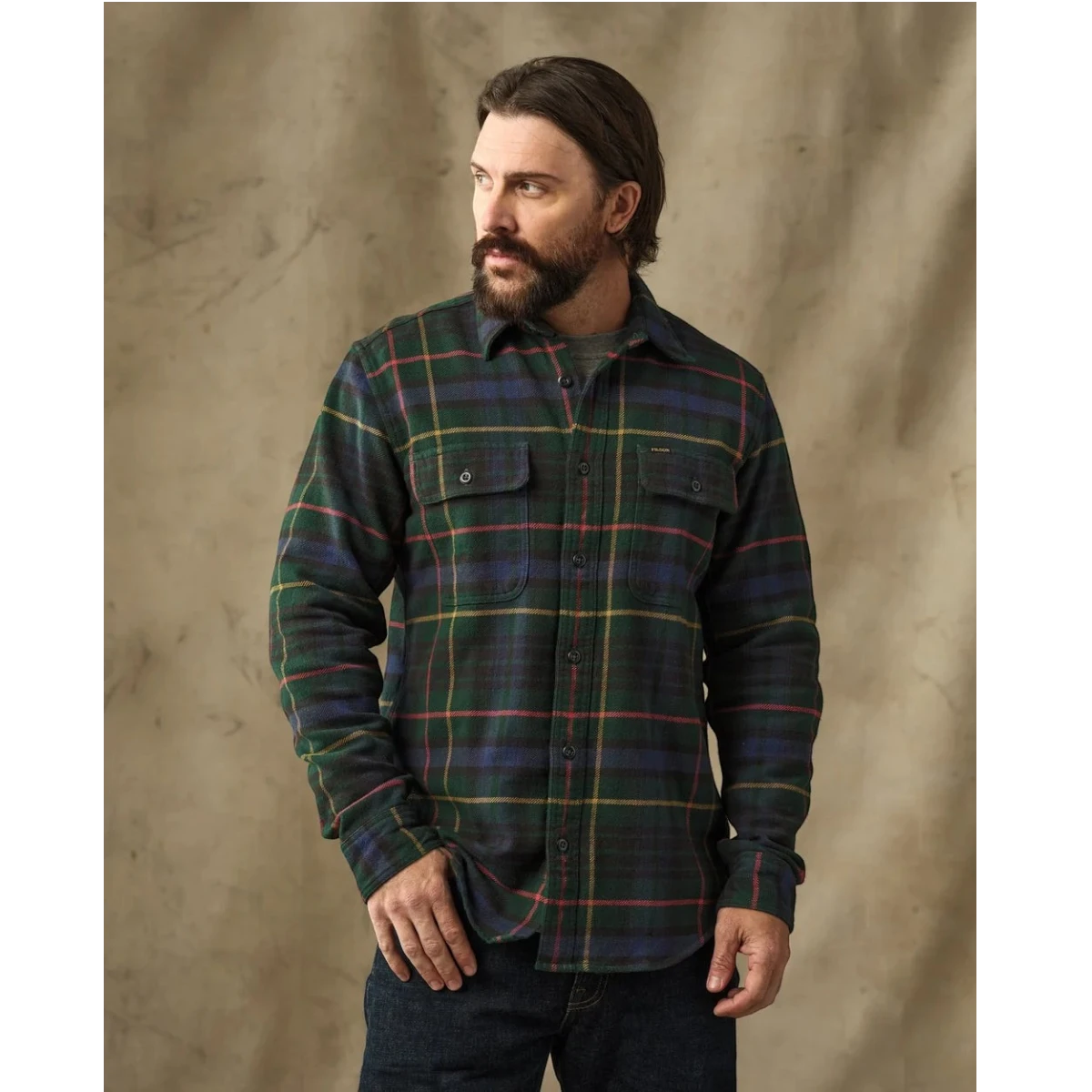 MILWORKS Filson vintage green and navy plaid flannel work shirt with button-flap pockets worn by a bearded man.