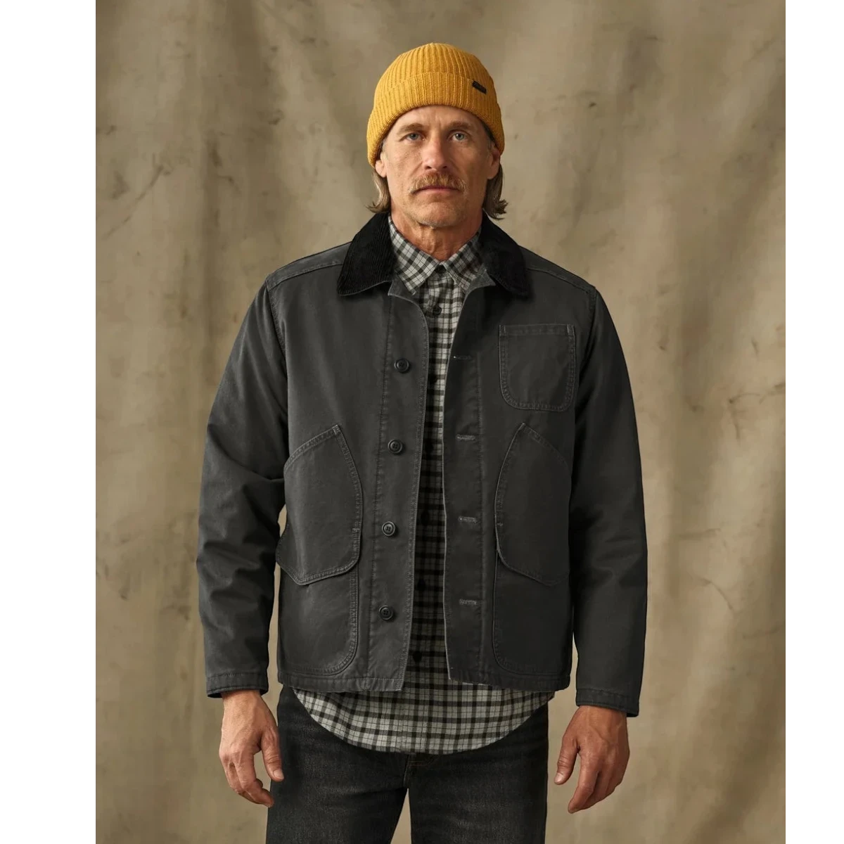 MILWORKS Filson insulated canvas outfitter jacket in peat green with a corduroy collar worn by a man in a yellow beanie