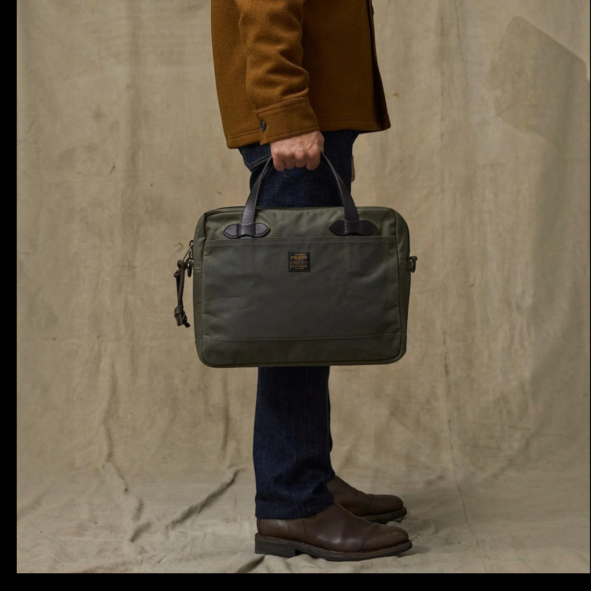 MILWORKS Filson Tin Cloth Compact Briefcase in Otter Green waxed cotton with Bridle Leather handles held by a man