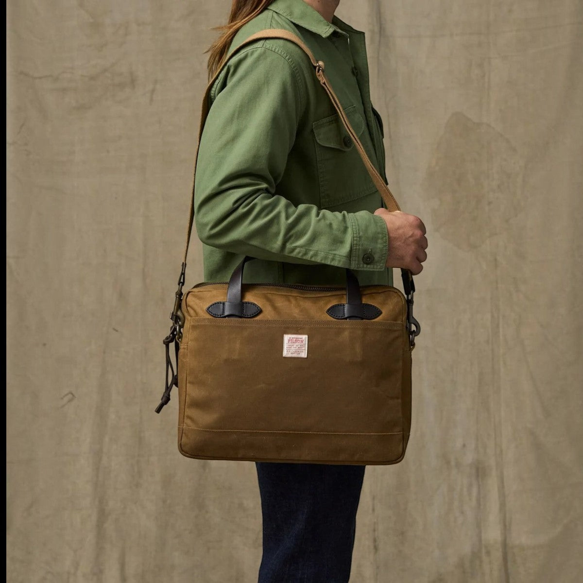 MILWORKS Filson dark tan waxed Tin Cloth compact briefcase with bridle leather handles worn over the shoulder.