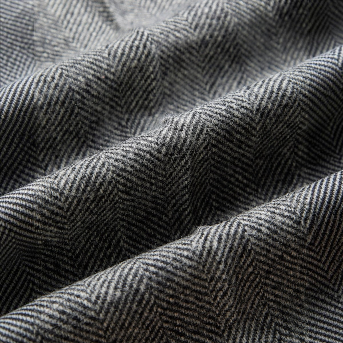 Close-up of MILWORKS grey herringbone virgin wool fabric with a textured weave pattern for single pleat trousers.