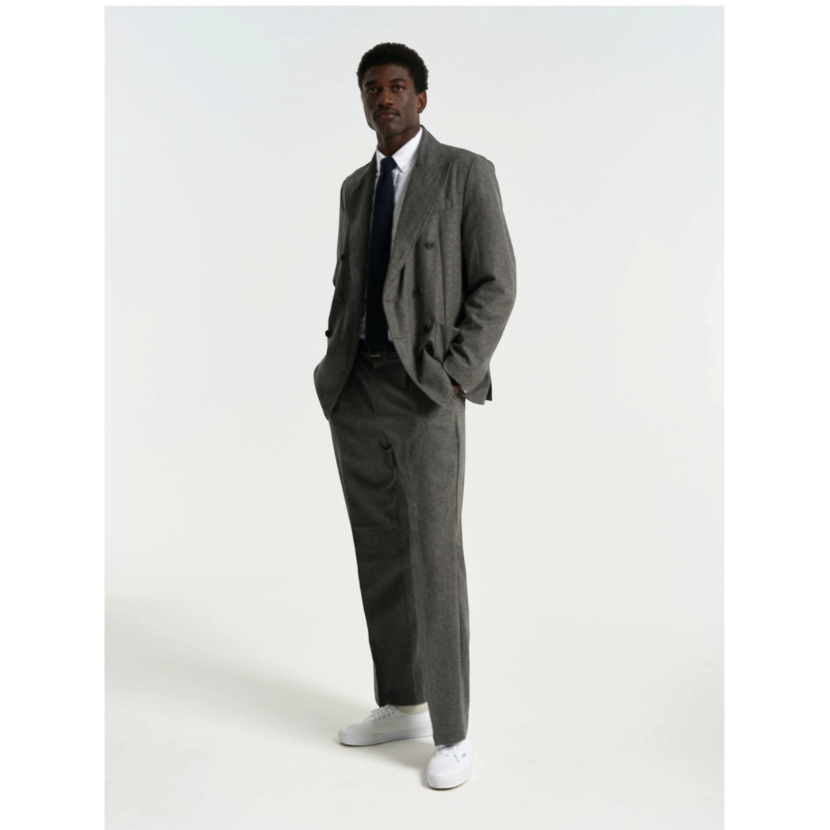 MILWORKS grey virgin wool single pleat trousers worn by a man in a matching blazer, white shirt, and white sneakers.