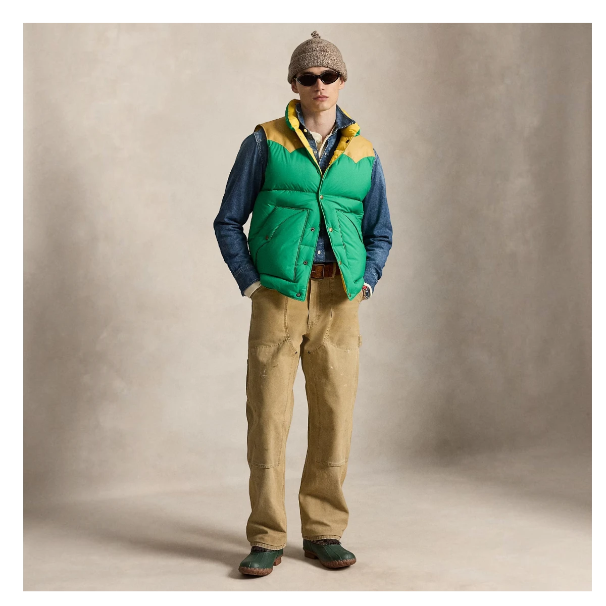 MILWORKS model wearing a green and yellow down vest with leather yoke over a denim shirt and tan work pants