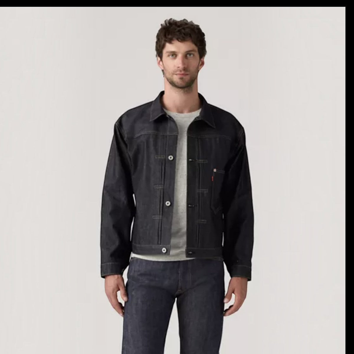 A man wearing a MILWORKS Levis Vintage Clothing WWII trucker jacket in dark rigid 13oz denim with a classic fit.