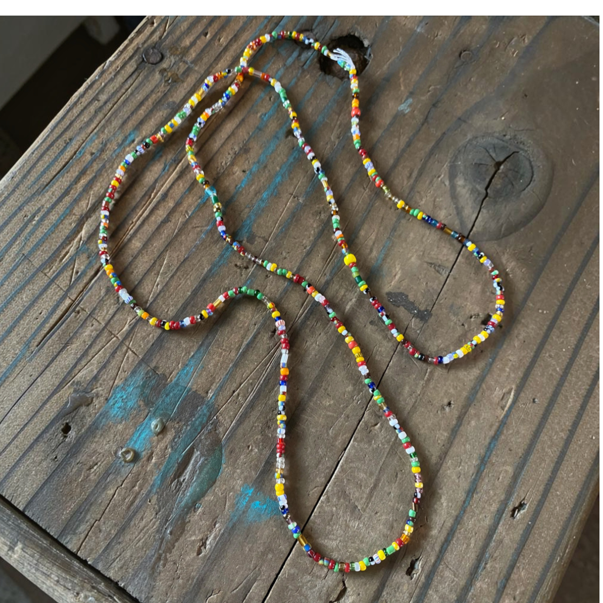 MILWORKS multicolored mini glass trade beads on cotton thread, 30-inch long layering necklace on rustic wood surface