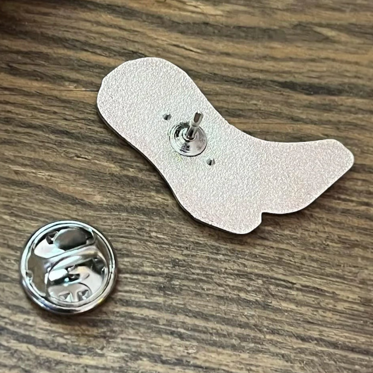 MILWORKS Peewee boot enamel pin back view showing the metal post and clutch fastener on a wooden surface
