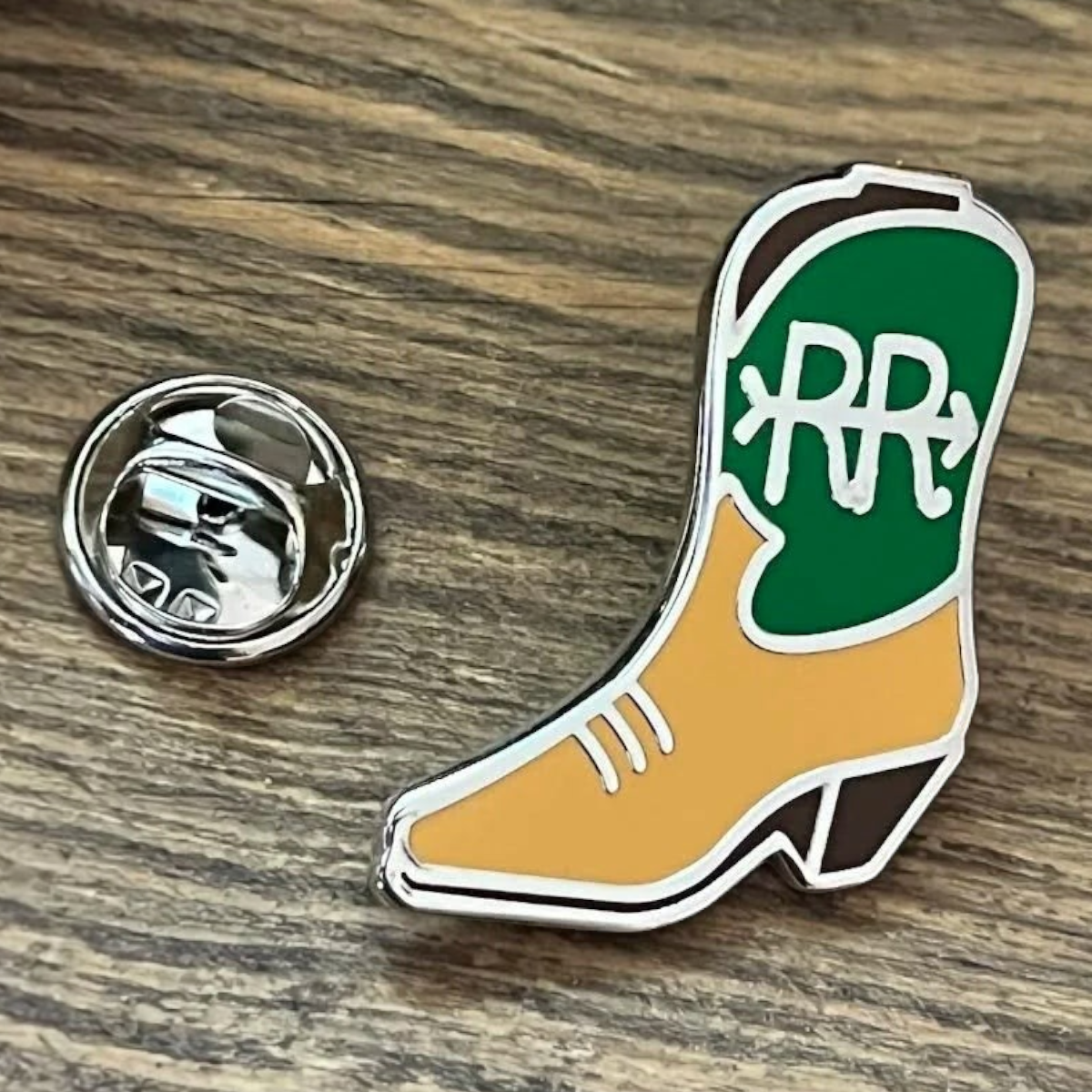MILWORKS Peewee cowboy boot enamel pin in green, yellow, and brown with RR logo on a wooden surface.