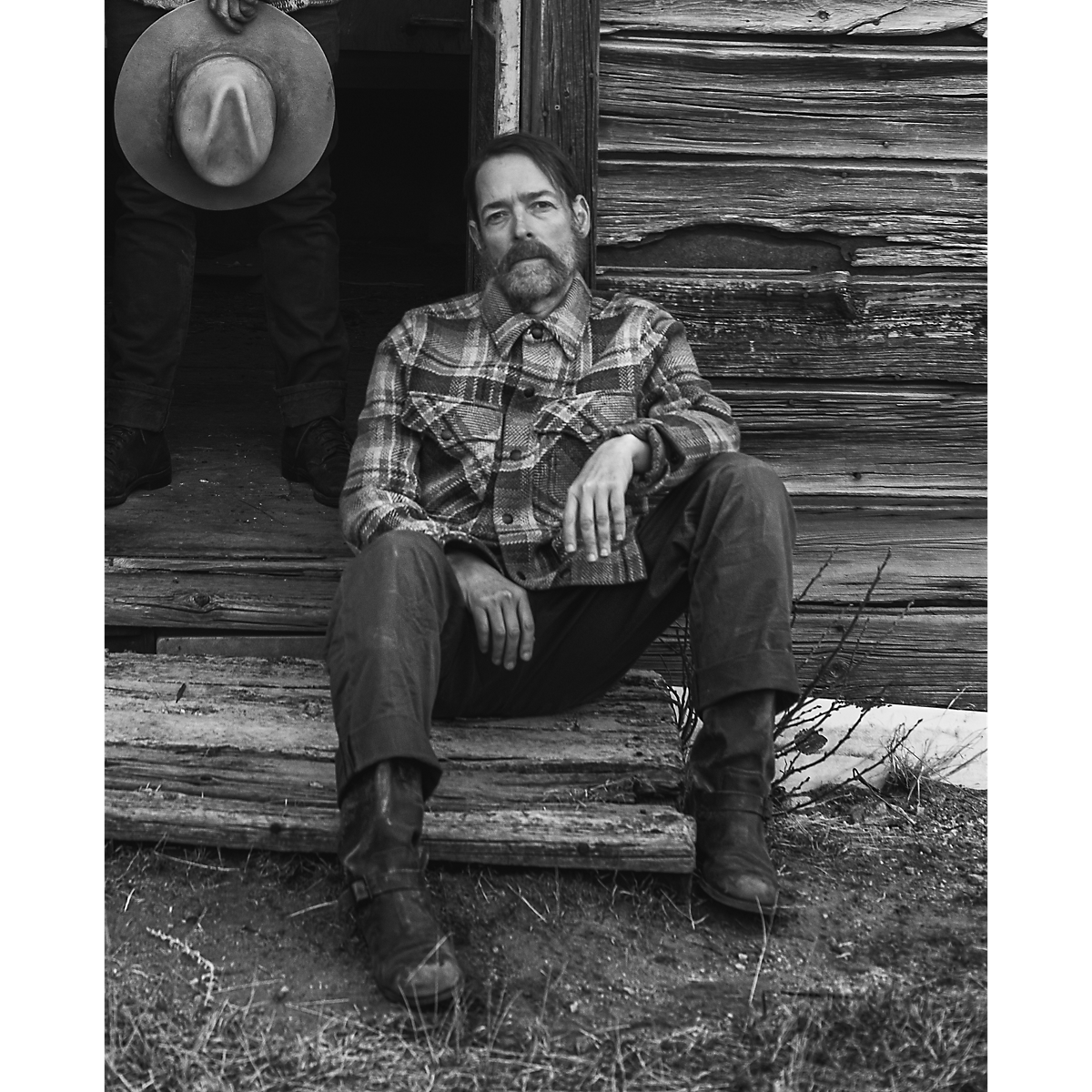 MILWORKS model wearing a tan and rust plaid RRL wool workshirt sweater while sitting on rustic wooden steps