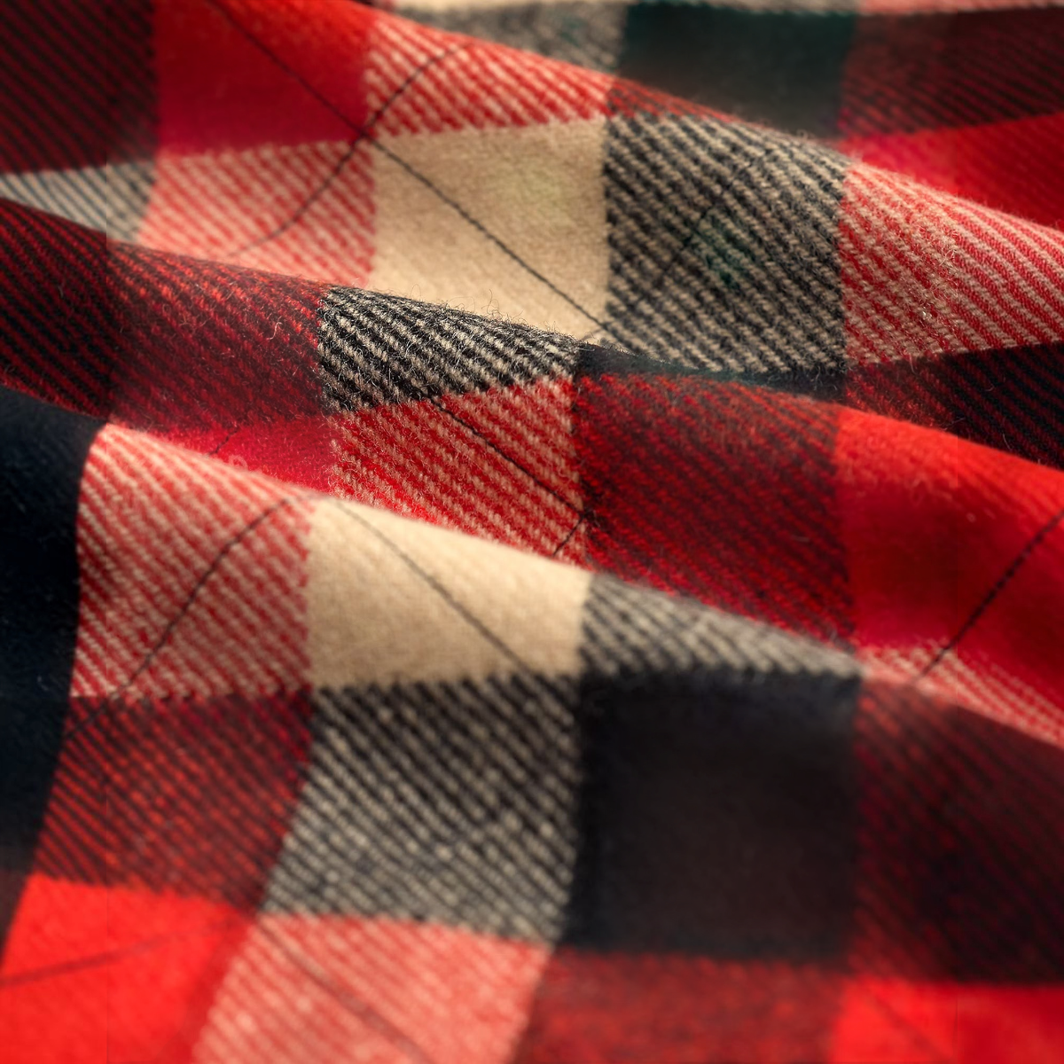 Close-up of MILWORKS quilted red and black plaid wool twill fabric with visible stitching and soft texture.