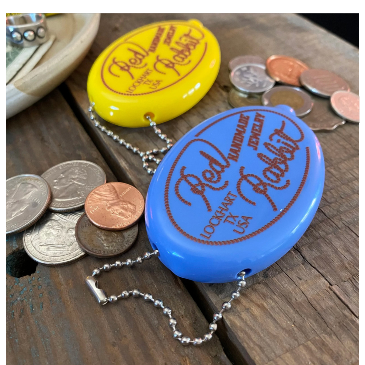 MILWORKS Red Rabbit coin keeper squeeze pouches in steel blue and bright yellow with metal chains on a wooden table.