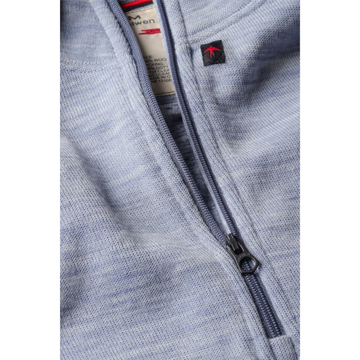 Close-up of a MILWORKS Relwen light blue wool cotton quarter zip sweater featuring a dark zipper and brand label.