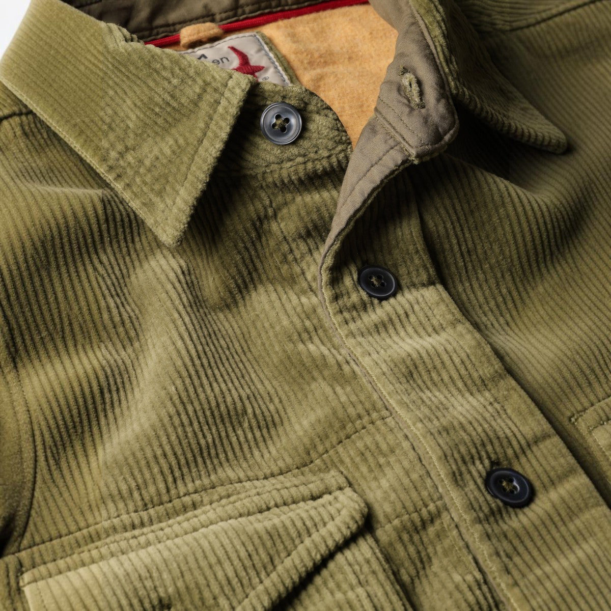 Close-up of a MILWORKS Relwen corduroy workshirt in moss green with dark buttons and a soft interior lining.