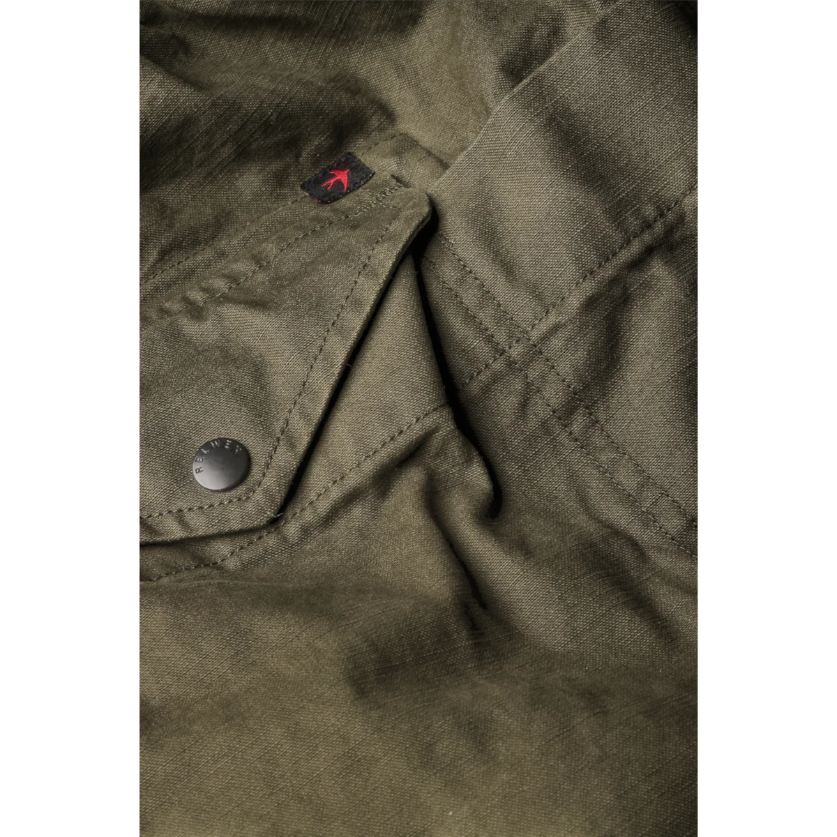 Close-up of MILWORKS Relwen olive drab canvas utility pant featuring a snap button pocket and red bird logo tag.