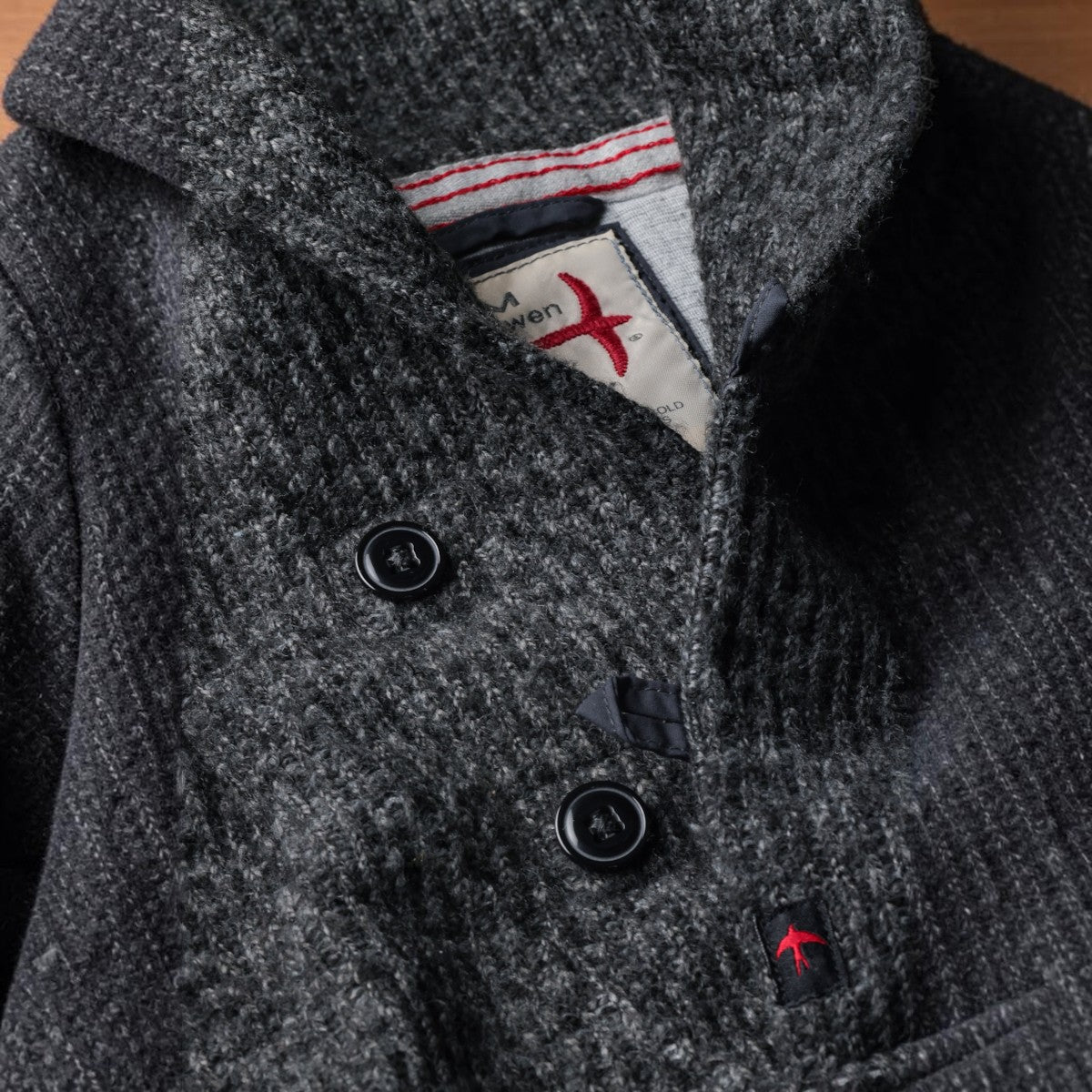 MILWORKS Relwen Ridge Twist shawl collar sweater in charcoal grey knit with black buttons and branded label detail.