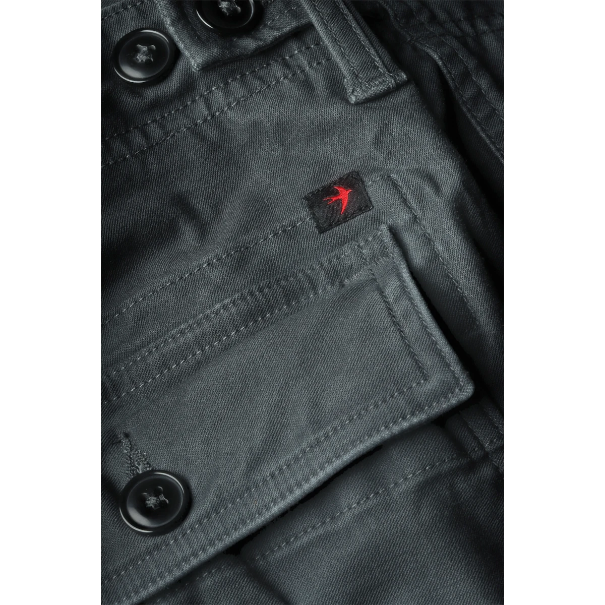 Close-up of MILWORKS Relwen Supply Pant in steel grey featuring durable cotton fabric and a red bird logo patch