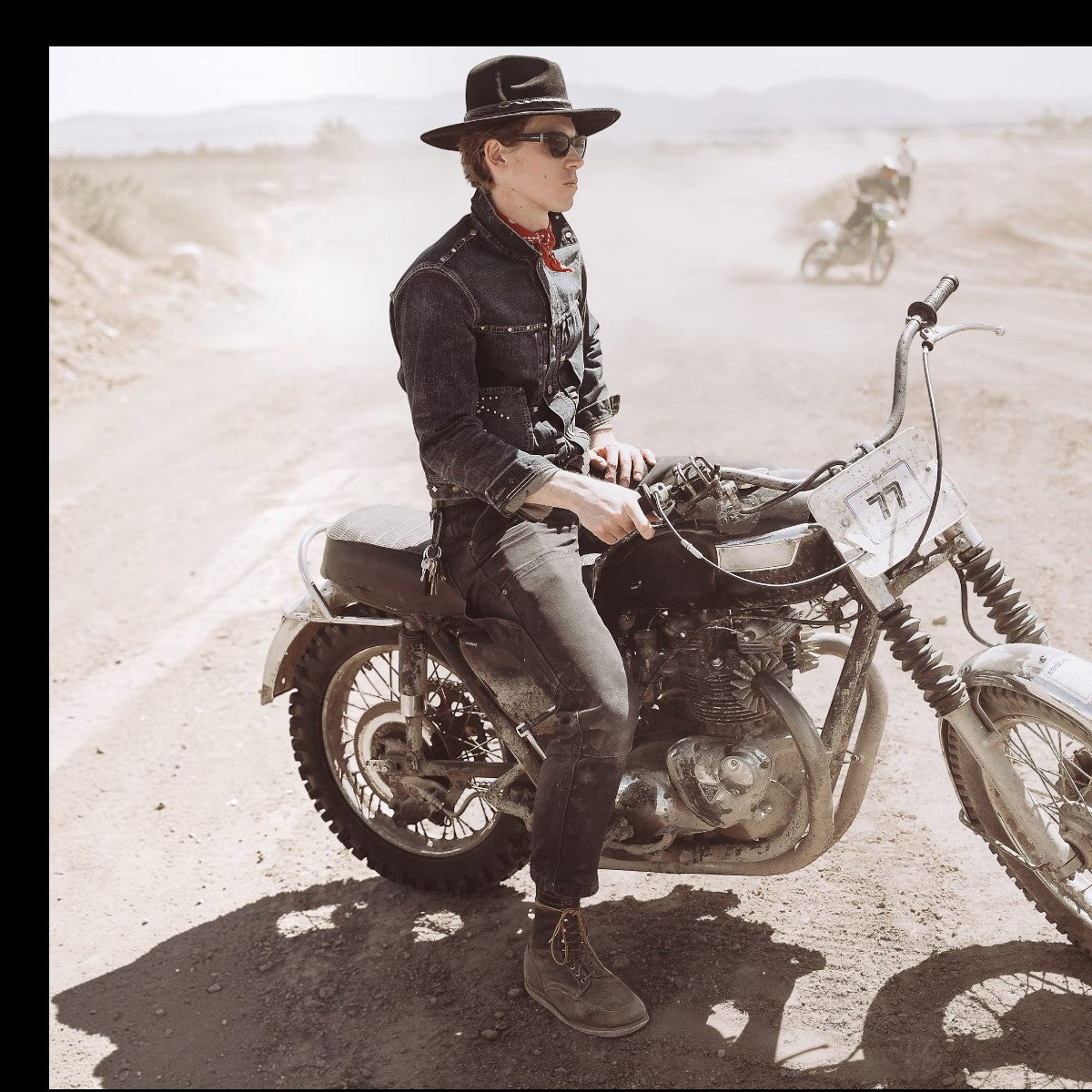 MILWORKS Ridgewood studded indigo denim trucker jacket worn by a man on a vintage motorcycle in a dusty desert setting