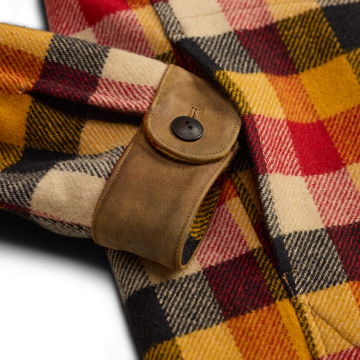 Close-up of a MILWORKS RRL wool woven shirt featuring a yellow and red plaid pattern with a brown leather cuff detail.