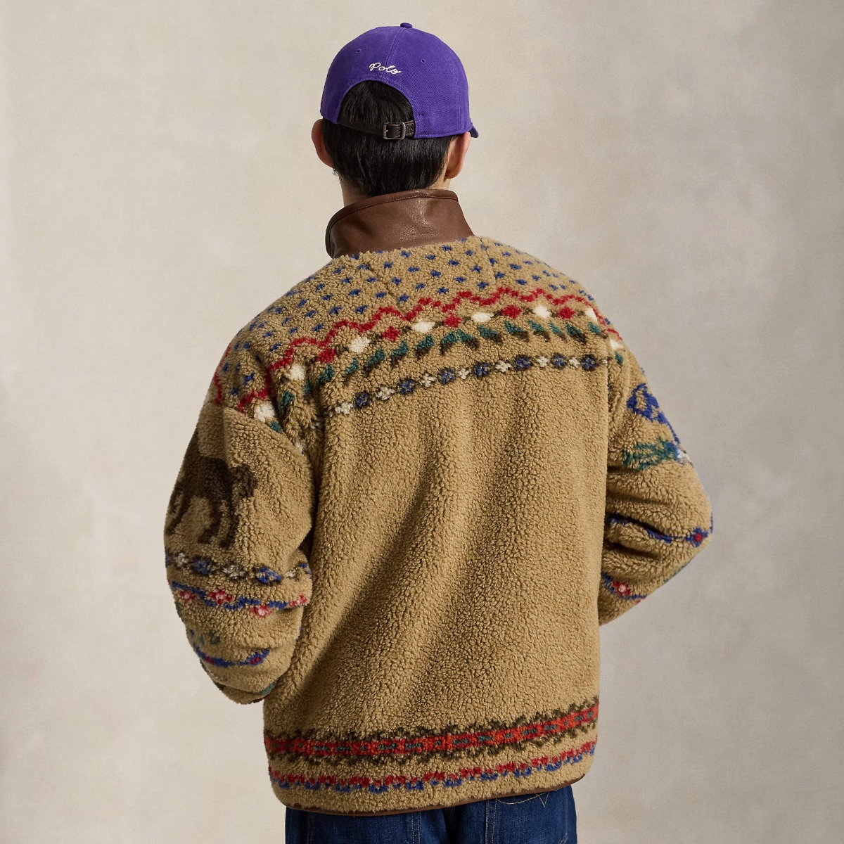 Back view of a man wearing a MILWORKS Scenic Pile Fleece Jacket in Montana Khaki with geometric motifs and leather trim