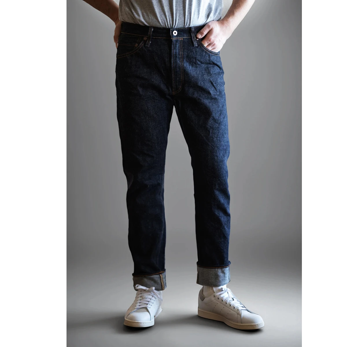 MILWORKS men's slim fit dark indigo 17oz selvedge denim jeans, cuffed, worn with white sneakers.