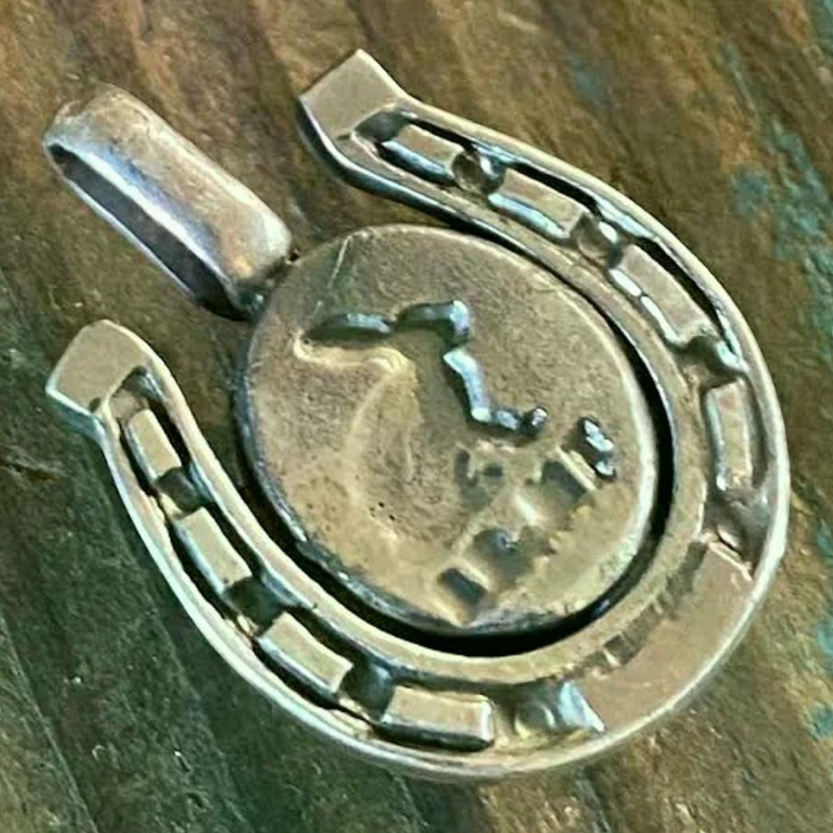 MILWORKS sterling silver horseshoe charm featuring a central oval turquoise stone on a rustic wooden background.