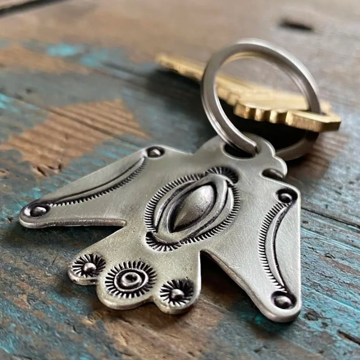 MILWORKS white bronze Thunderbird keychain featuring intricate repousse and sunburst stamping on a rustic wood surface.